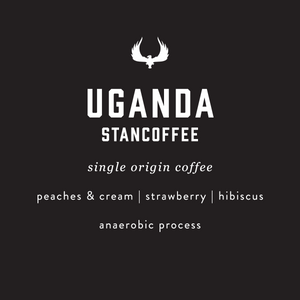 A dark charcoal graphic with white text reading 'UGANDA STANCOFFEE' and smaller text below including 'single origin coffee', 'peaches & cream | strawberry | hibiscus', and 'anaerobic process'. A white stylized bird logo appears above the main text.